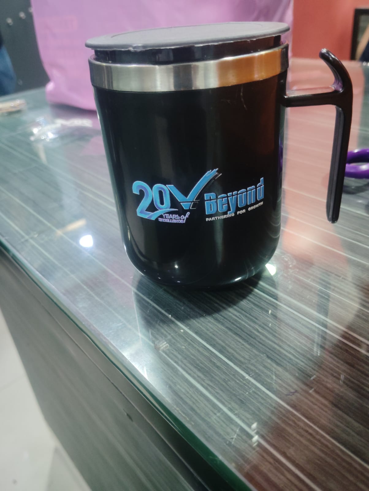 Black steel coffee mug with lid, printed with a blue 20 years anniversary logo